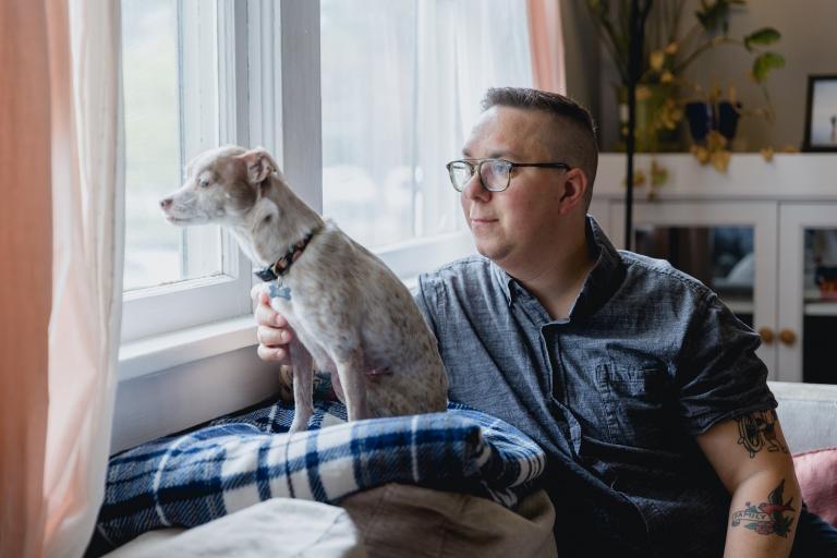 Man met hond kijkt vanuit woonkamer uit raam 